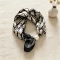 Primo piano di foulard in seta nero e bianco con motivo monogramma di lusso e fibbia di perla. - Lettere di Lusso