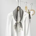 Detailed view of black and white striped silk scarf with wooden magnetic ring on white blazer. - CXK010-Beige Fret Pattern