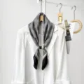 Detailed view of black and white houndstooth silk scarf with magnetic buckle on white blazer. - CXK010-Houndstooth