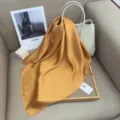 Detailed shot of solid golden satin silk scarf in elegant display scene with bag and decor. - Yellow