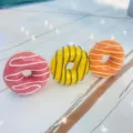Nahaufnahme von drei bunten Donut-Handyhaltern in Pink, Gelb und Orange, sehr realistisch. - Erweiterbarer Ständer / Gelber Donut