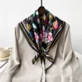 Detail view of a black square silk scarf featuring colorful tulip floral print and striped border. - Black