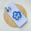 Close-up detail of a blue acrylic flower shaped phone socket grip mounted on a light blue smartphone - Support / Blue Flower
