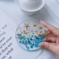 Macro detail of clear resin coaster featuring blue stones, gold foil, and starfish charm - Blue Ocean Round Coaster