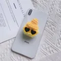 Detailopname van gele pluchen haarbal telefoonhouder met hoed en hartjesbril - Pompon Muts Houder / Geel