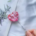 Detailansicht eines glitzernden Herz-Ausweishalters mit ausziehbarer Kordel in der Hand - Rosa Sechseck-Pailletten (Nr. 7)