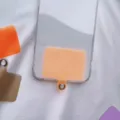 Detail view showing an orange universal phone tether tab inside a clear phone case. - Orange Card