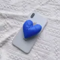 Detailaufnahme eines blauen, gepolsterten Herz-Handyhalters aus Stoff auf einem Handy - Erweiterbarer Ständer / Saphirblau