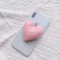 Nahaufnahme eines rosafarbenen Herz-Handy-Griffs aus Stoff auf einem weißen Smartphone. - Erweiterbarer Ständer / Hellrosa