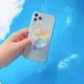 Nahaufnahme eines süßen regenbogenfarbenen Bären-Handyhalters vor strahlend blauem Himmel - Erweiterbarer Ständer / Regenbogen Bär Stil 4