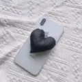 Nahaufnahme einer schwarzen Herz-Handyhalterung aus Stoff auf einem weißen Smartphone - Erweiterbarer Ständer / Schwarz