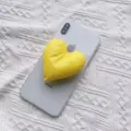 Nahaufnahme eines leuchtend gelben, herzförmigen Stoff-Handyhalters auf einem Smartphone - Erweiterbarer Ständer / Gelb