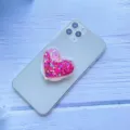 Detaillierte Nahaufnahme eines rosa glitzernden Herz-Quicksand-Handygriffs am Smartphone - Erweiterbarer Ständer / Rosarotes Herz Treibsand