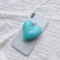 Detailansicht eines weichen, türkisfarbenen Herz-Handyhalters aus Stoff auf einem Smartphone - Erweiterbarer Ständer / Blau