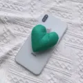 Detailansicht eines grünen herzförmigen Handy-Griffs aus Stoff auf einem weißen Smartphone - Erweiterbarer Ständer / Grün