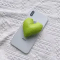 Nahaufnahme einer grünen herzförmigen Handyhalterung aus Stoff am Smartphone. - Erweiterbarer Ständer / Hellgrün