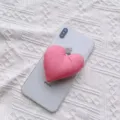 Detaillierte Nahaufnahme einer weichen rosa herzförmigen Stoff-Handyhalterung auf einem Handy - Erweiterbarer Ständer / Dunkelrosa