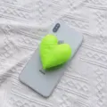 Neongrüner herzförmiger gepolsterter Stoff-Handygriff an einem weißen Smartphone - Erweiterbarer Ständer / Fluoreszierendes Grün