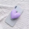 Nahaufnahme einer weichen lila herzförmigen Handyhalterung auf einem weißen Smartphone - Erweiterbarer Ständer / Lila