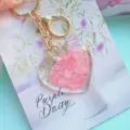 Macro detail of heart-shaped resin keychain with real pink dried flowers and gold foil. - Pink Petal