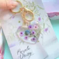 Detailaufnahme von echten violetten Trockenblumen in einem herzförmigen Schlüsselanhänger aus Harz - Lila Blumen