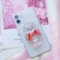 Dettaglio ravvicinato di un supporto per telefono a forma di orsetto trasparente con fiocco rosso. - Supporto a gonfiabile / Orso con Fiocco Rosso