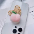Close-up of a 3D pink peach squishy phone grip holder on a clear iPhone case background - Peach Heart Style