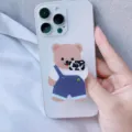 Detailaufnahme eines niedlichen Cartoon-Bären Acryl-Handyhalters auf einem weißen Smartphone - Erweiterbarer Ständer / Kamera-Bär