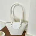Borsa a secchiello bianca minimalista con tracolle lunghe e borchie dorate sottobraccio. - senza ciondolo / Bianco