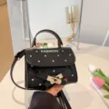 Elegant black polka dot handbag featuring a classic gold buckle closure and top handle strap - Black