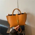 Elegante bolso cubo de cuero granulado marrón con cierre dorado y asas. - Marrón