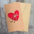 Biglietto d'auguri vintage in carta kraft con cuore intagliato al laser e busta coordinata. - Fiocco con Motivo a Cuore