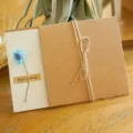 Biglietto di auguri vintage in carta kraft con fiore secco blu e nodo in corda rustica - Margherita Blu (Fiore Artificiale)