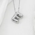 Gros plan détaillé d'un pendentif lettre argenté gonflé tendance, finition lisse, chic. - Lettre E