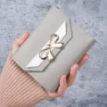 Elegant grey short wallet for women featuring a gold bow decoration and white flap - Gray
