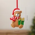 Christmas resin bear ornament wearing Santa hat and scarf holding a green gift box - Gift Bear