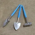 Mini gardening tool detail view featuring metal shovel and rake with blue plastic handles - Three-Piece Set / Blue