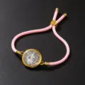 Detailed close-up view of a pink braided rope bracelet with a vintage gold coin pendant - Bracelet / Pink