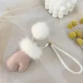 Macro detail of cute pink mitten-shaped bag charm with white fluffy mink fur pom-poms - Pink White