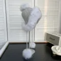 Detalle de gorro de invierno de punto gris con ribete de piel de zorro y pompones suaves - Talla única / Zorro Azul Natural