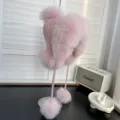 Vista lateral de un gorro ushanka rosa de piel sintética con pompones suaves - Talla única / Rosa loto