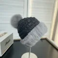 Close-up of black quilted winter hat with grey fur trim and large fluffy pom-pom - One Size / Grey Black