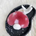 Cute red plush mushroom keychain with white spots and golden ring on black ceramic display tray - Rose Pink