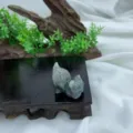 Close-up detail view of a hand-carved natural crystal cat figurine resting on wooden stand. - Labradorite / 3cm / Gray