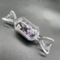Detailaufnahme einer klaren Glasflasche in Bonbonform, gefüllt mit lila Amethyst-Steinen. - Amethyst