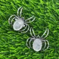 Close-up detail of silver spider pendant brooch with clear crystal oval stone on green turf. - White Crystal