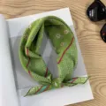 Detailed closeup of a green vintage floral patterned square scarf styled neatly on a wooden desk. - Picture #14