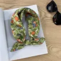 Detailed close-up of the green citrus and floral print scarf displayed on a wooden table. - Picture #19