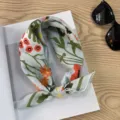 Detail shot of the pastel floral print cotton scarf styled neatly on a wooden tabletop. - Picture #12