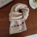 Detail view of cute embroidered wool scarf featuring cartoon characters and knit design. - Camel